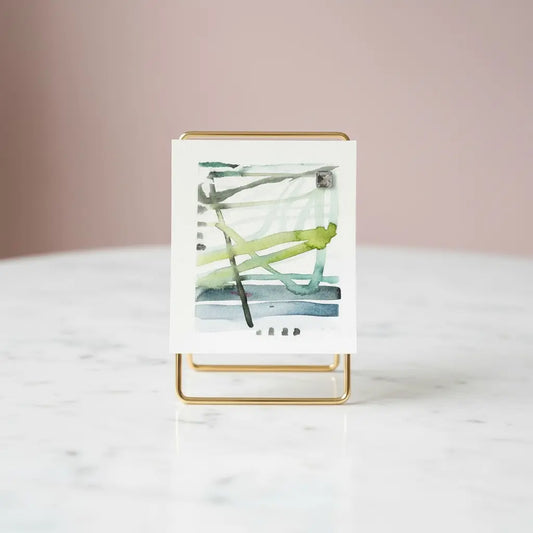 Small blue green watercolor painting on a stand against a neutral background blue current abstract mini watercolor painting