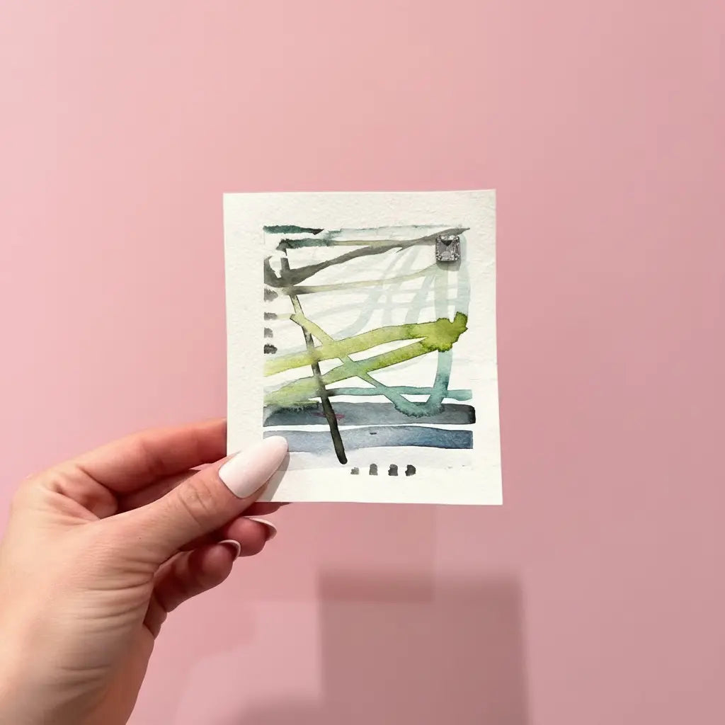 Hand holding a small watercolor painting against a pink background 