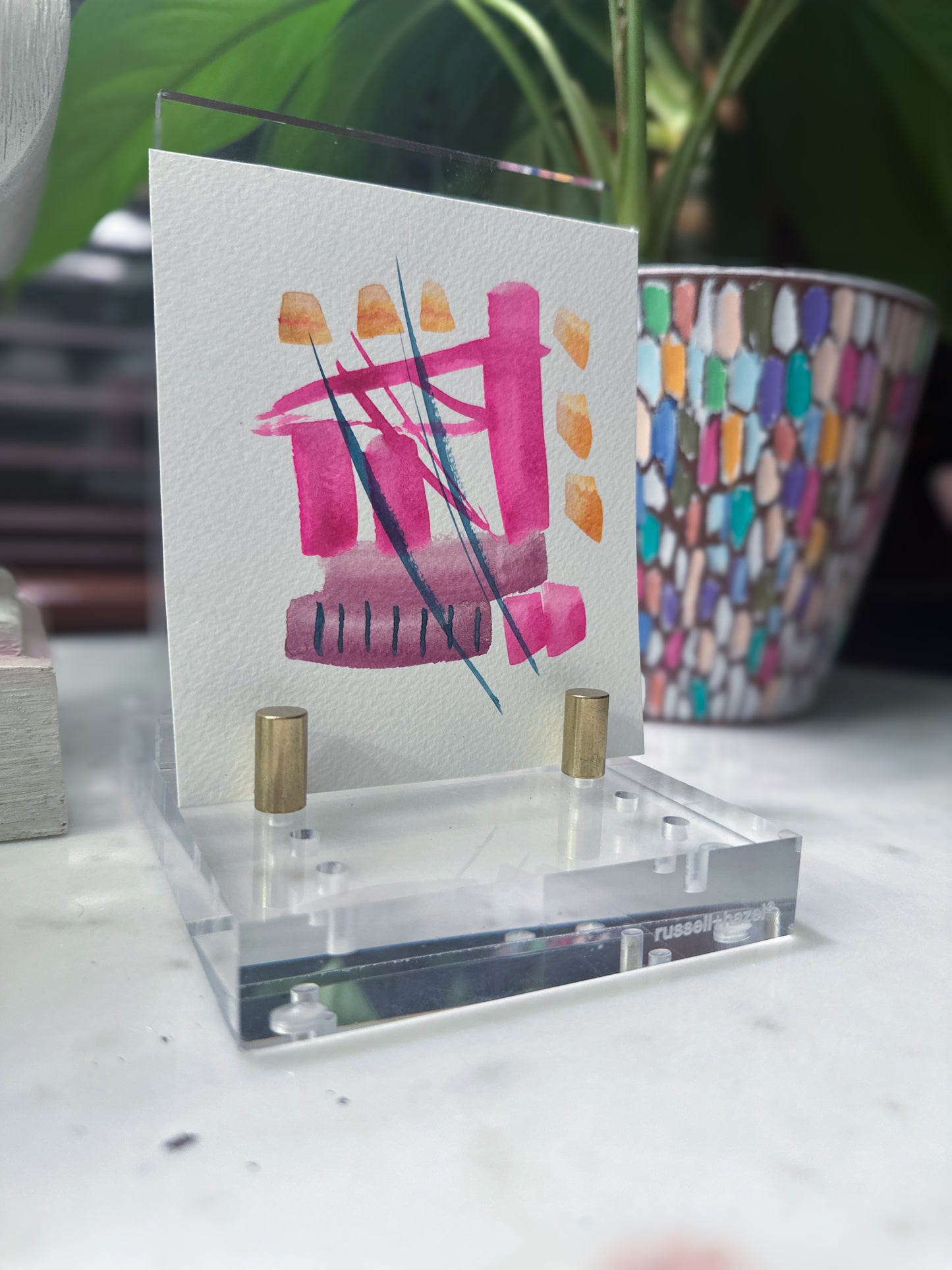 Acrylic stand with a card featuring a colorful design on a white surface. original pink abstract watercolor artwork styled on acrylic stand