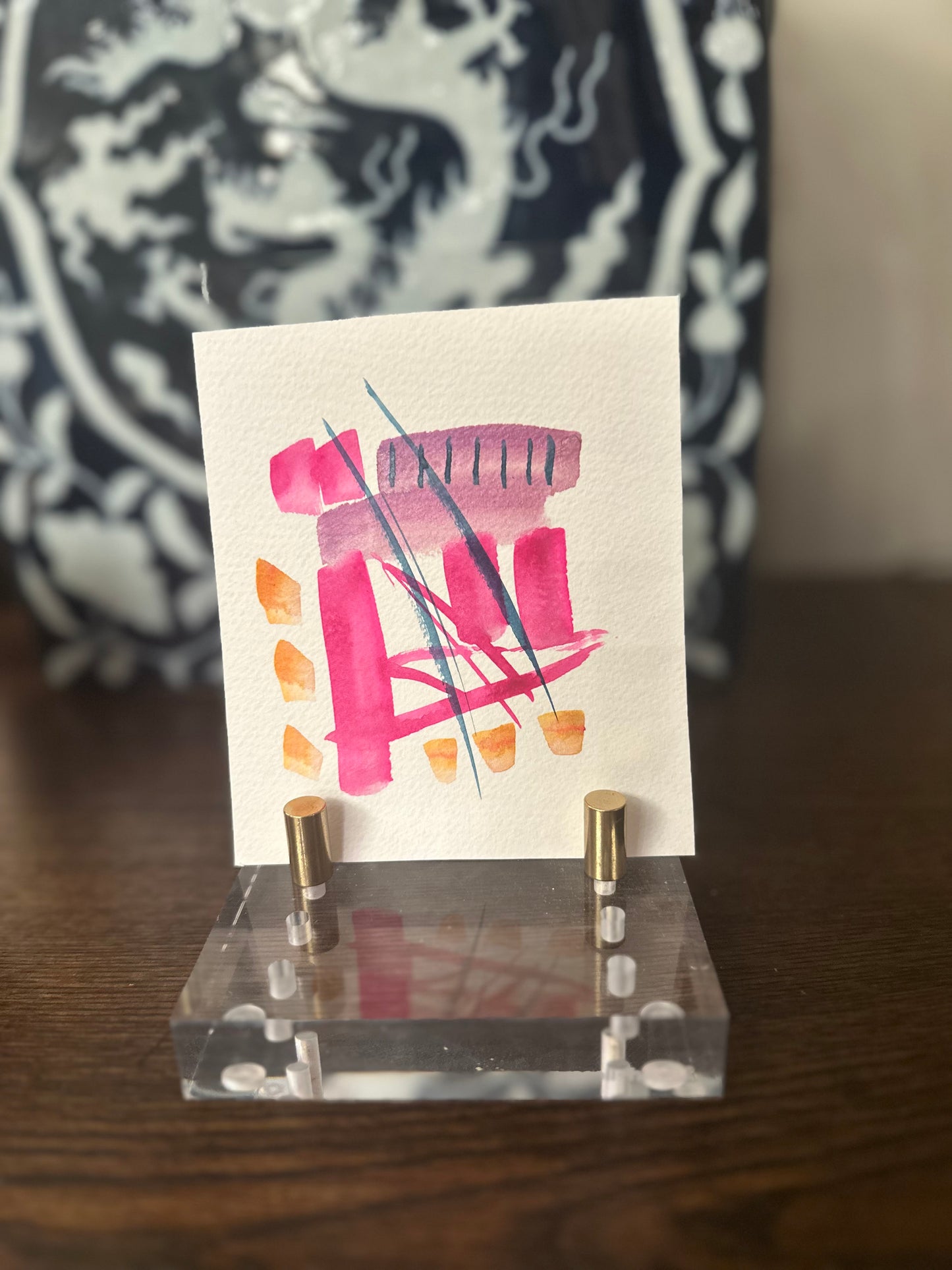 Small card with colorful design on a clear stand against a blurred background small pink abstract watercolor painting modern wall art